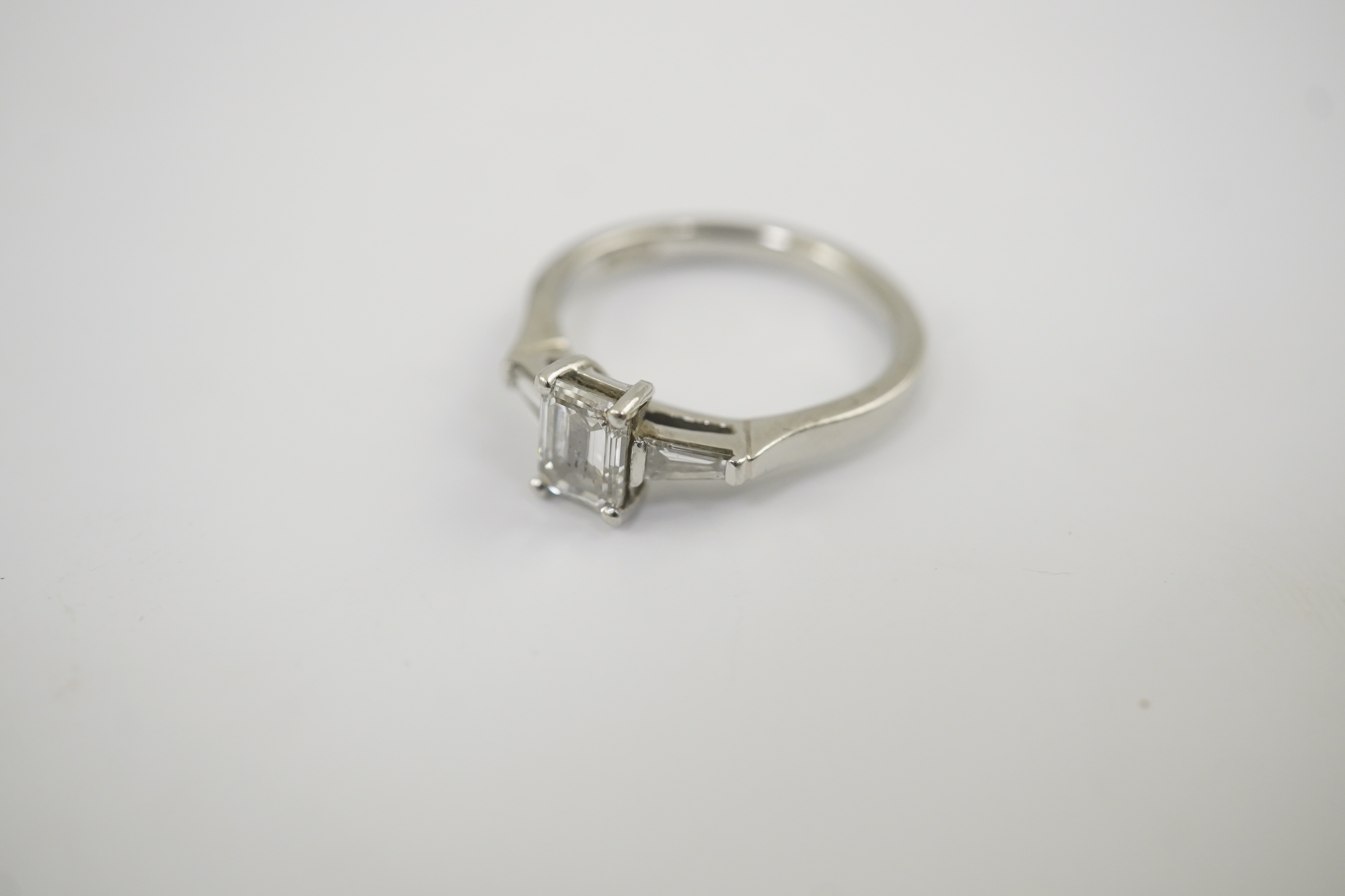 A modern platinum and single stone emerald cut diamond set ring, with two stone tapered baguette cut diamond set shoulders